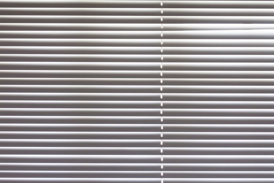 Close-up of horizontal window blinds indoors with natural light highlighting texture.